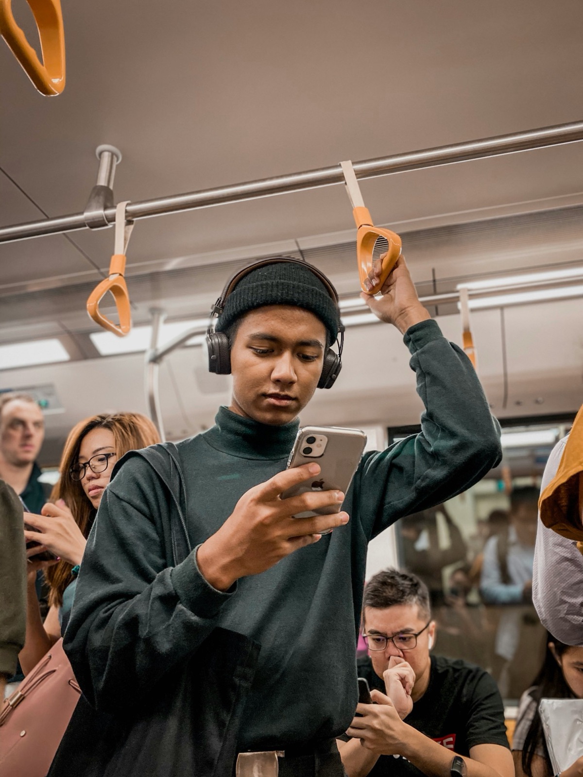 A commuter in headphones reads their phone while standing on a crowded train